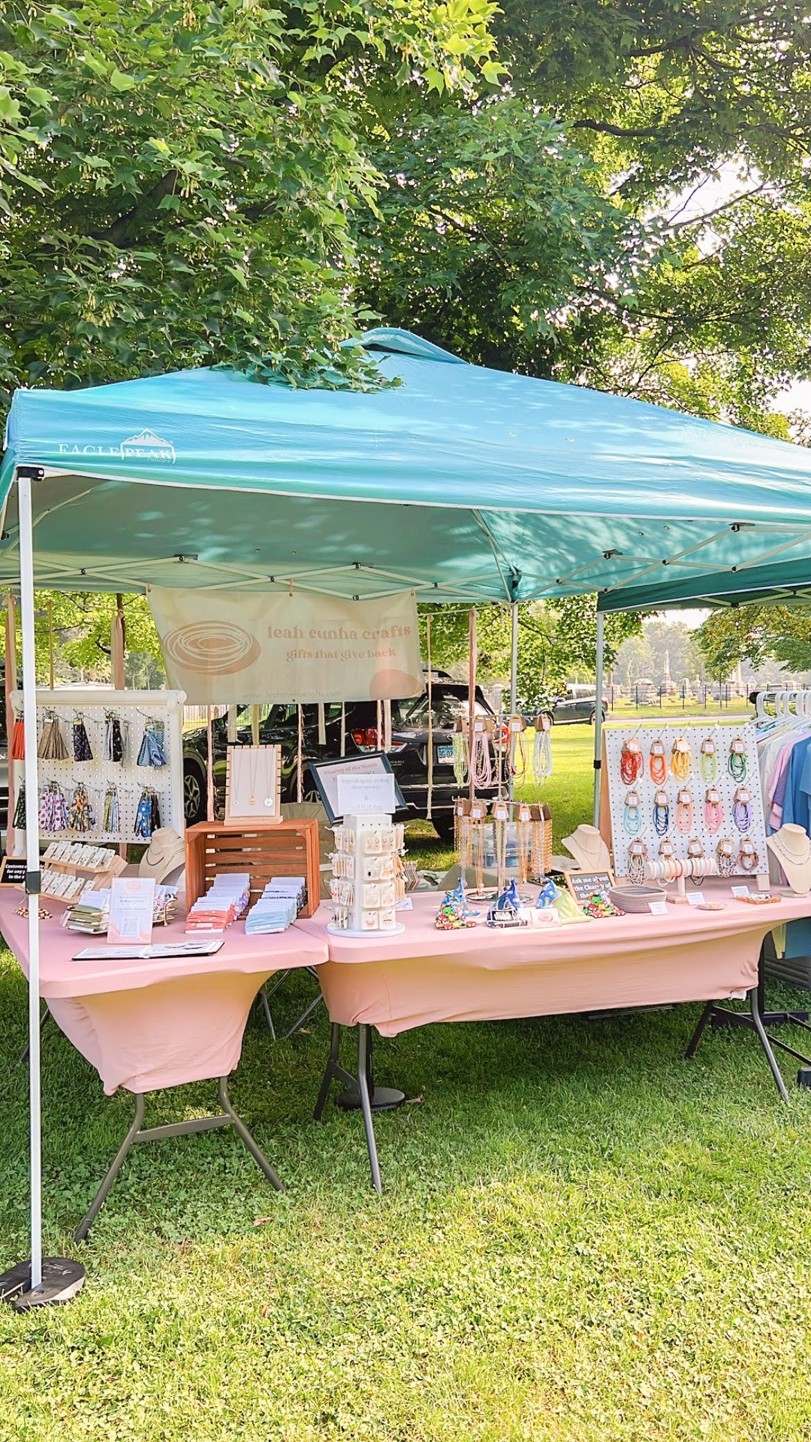 A craft fair booth with a blue tent, pink tablecloths, and lots of jewelry and accessories