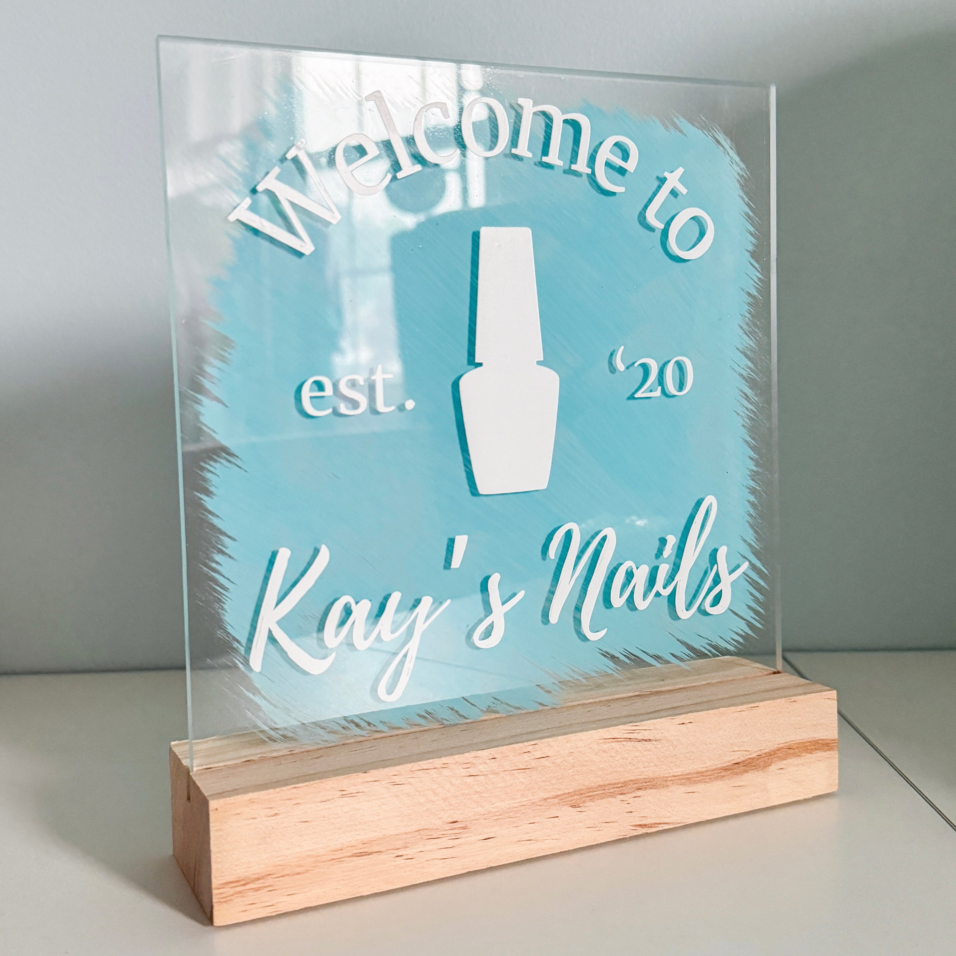 An acrylic sign with a nail salon logo in white with a blue paint background